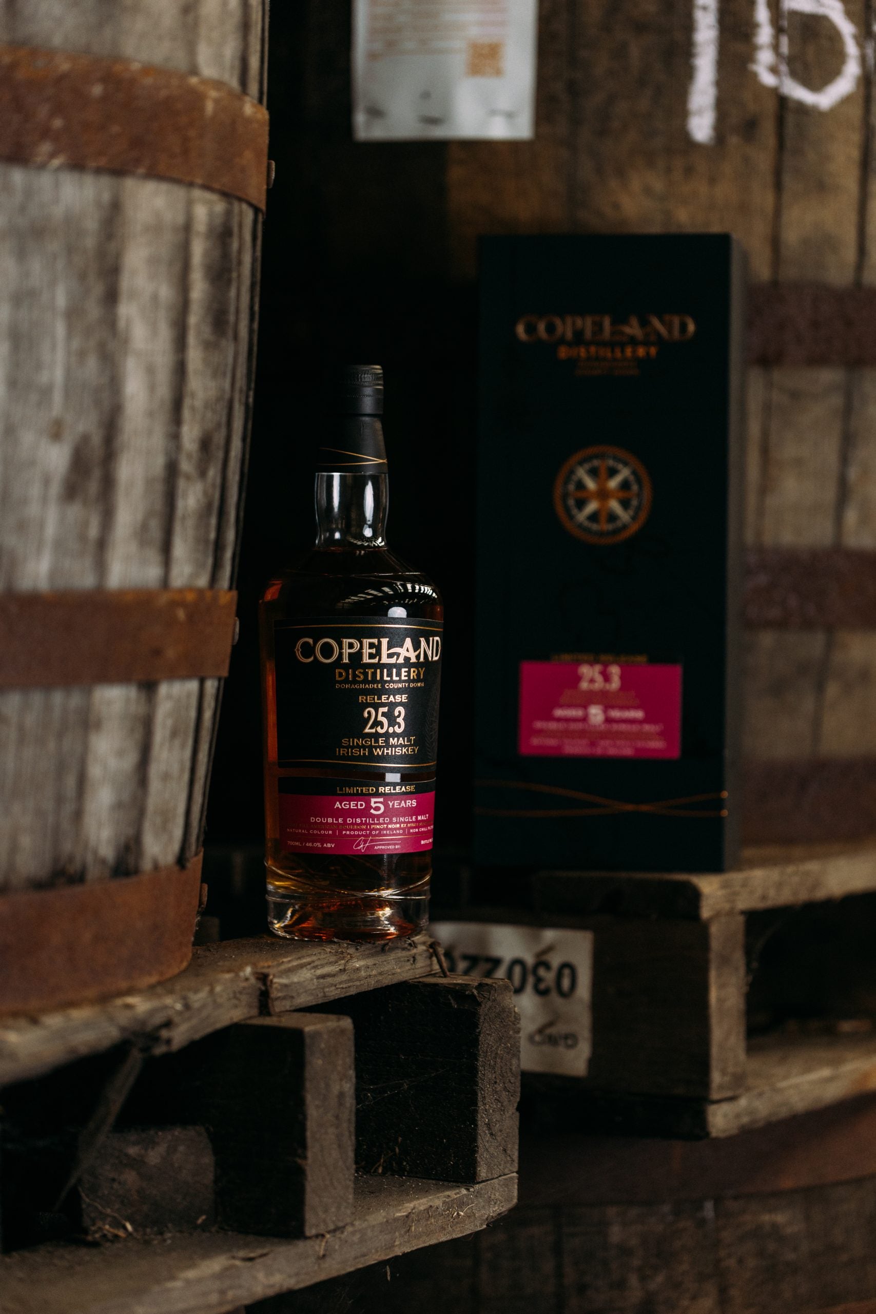 Copeland Distillery Release 25.3 Single Malt Irish Whiskey aged 5 years mit Geschenkverpackung vor Whiskyfässern